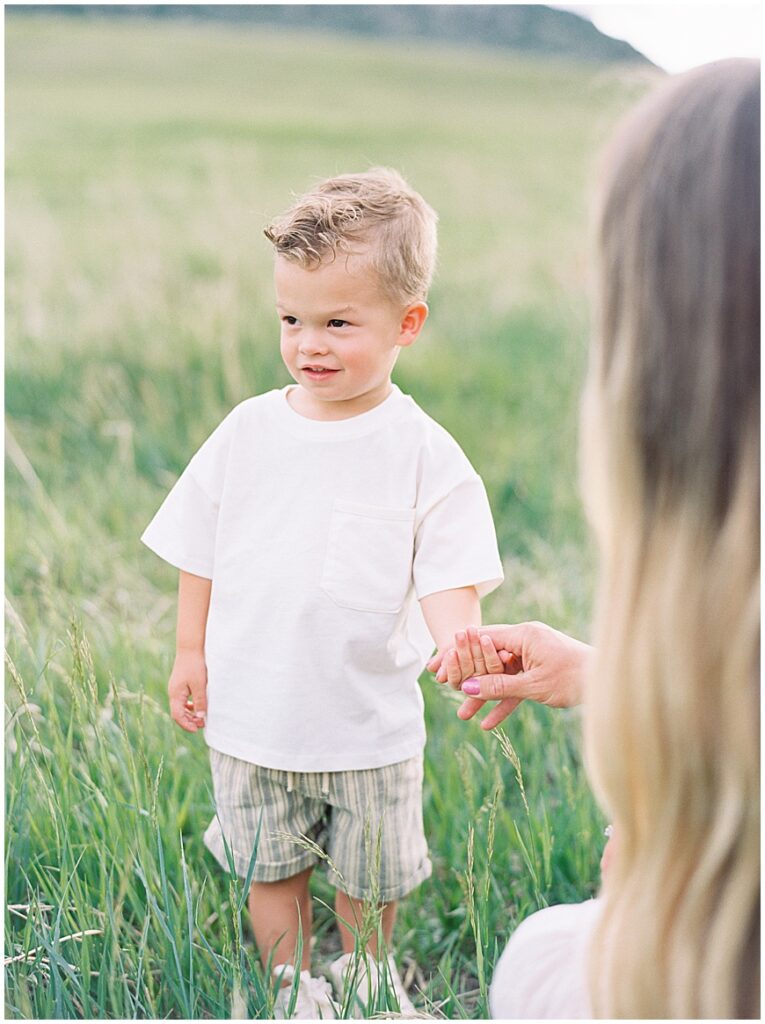 Family photoshoot of a little boy standing in field on path with mom.