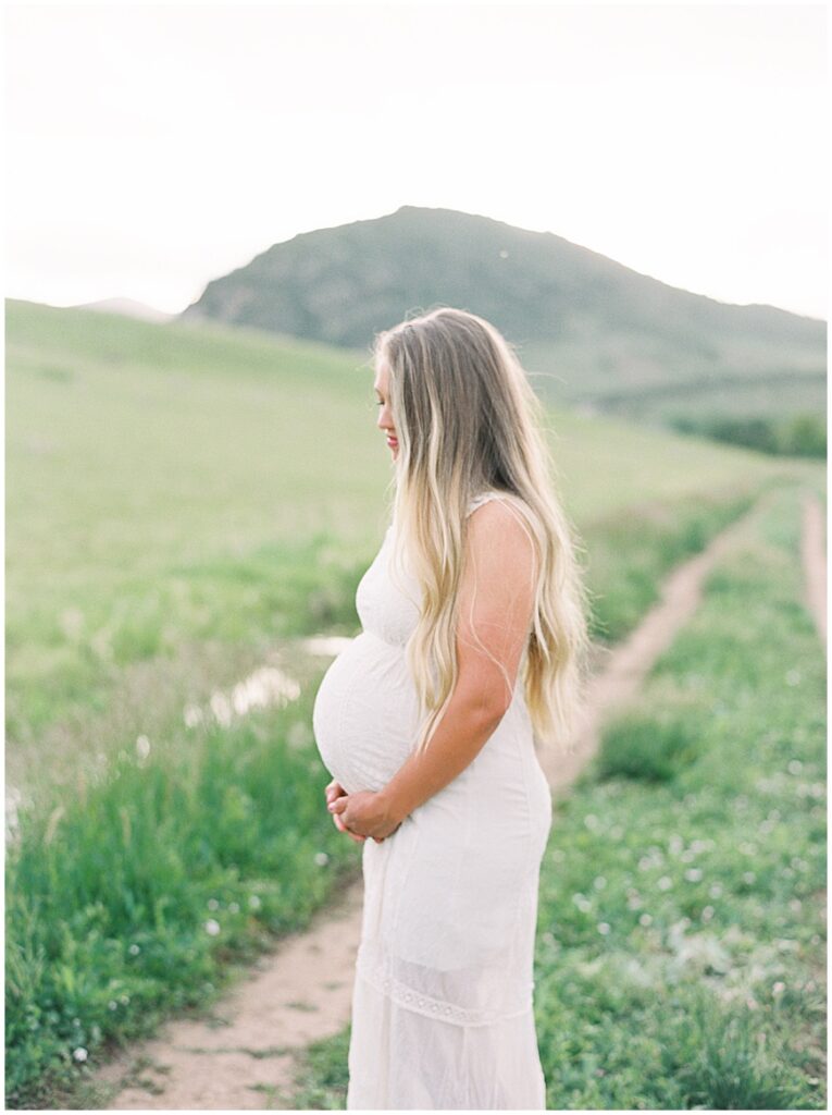 Family photography session of a pregnant woman standing in field on path.