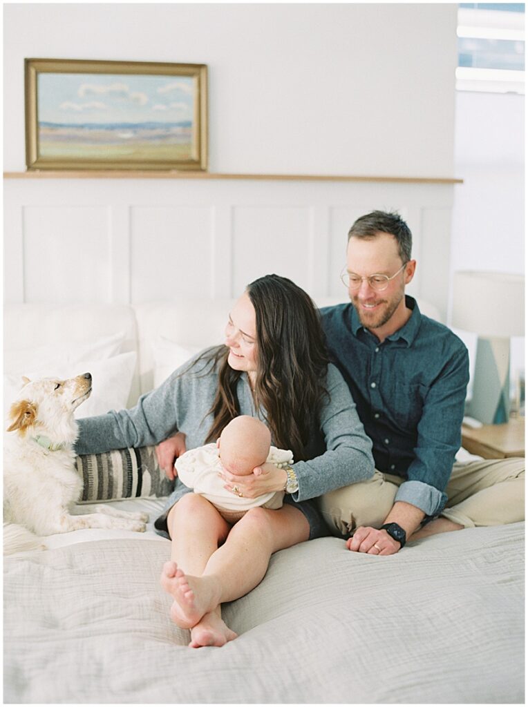 Mother & father holding baby in bedroom with dog during newborn session