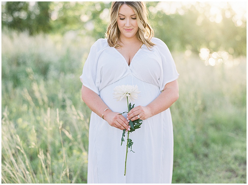 mother holding flowers in field during maternity session