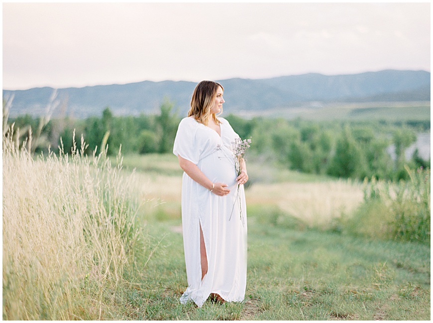 pregnant mother holding flowers in front of mountains in field during maternity session