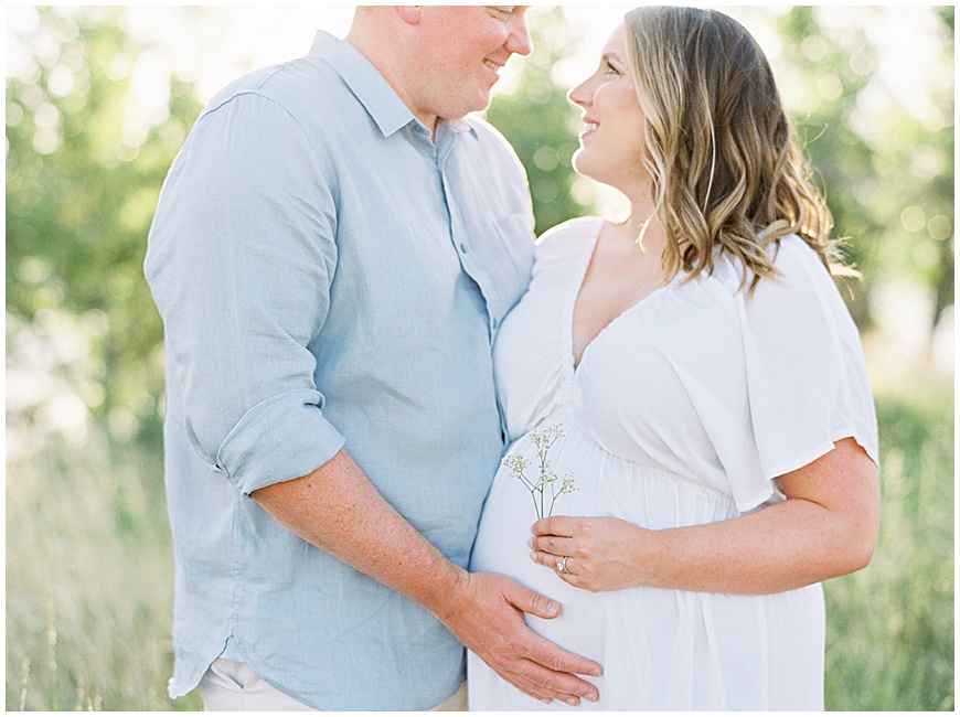 pregnant mother and father holding flowers in front of mountains in field during maternity session