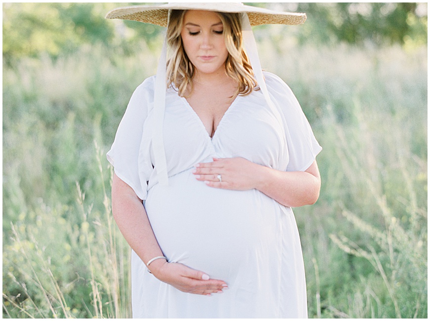pregnant mother wearing hat in front of mountains in field during maternity session